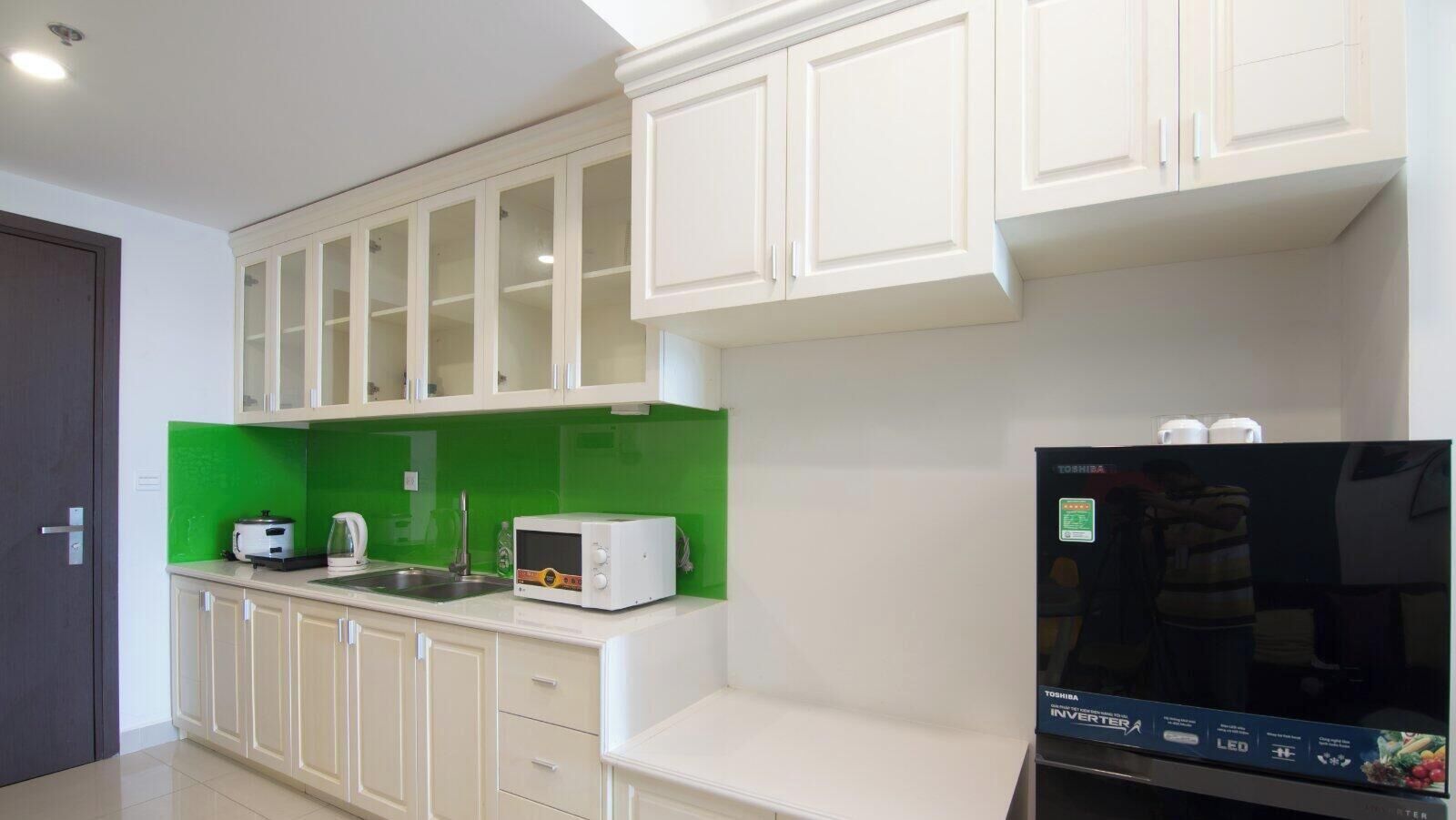 A kitchen with white cabinets, a green backsplash, a microwave, a toaster, and a refrigerator.