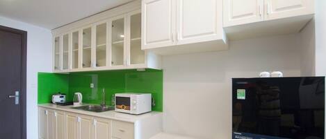 A kitchen with white cabinets, a green backsplash, a microwave, a toaster, and a refrigerator.