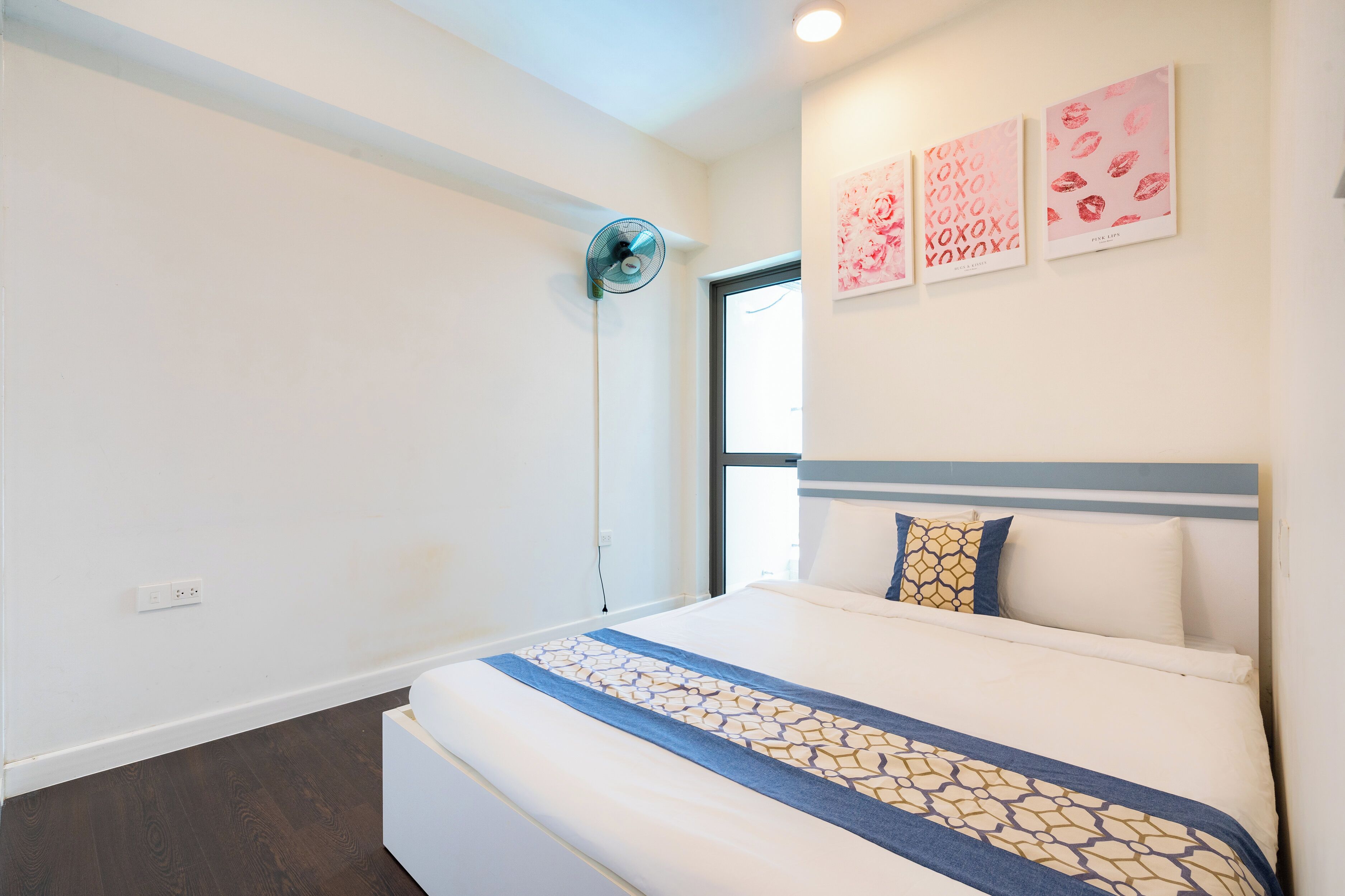 Een hotelkamer met een bed, een ventilator aan de muur en drie ingelijste foto's.