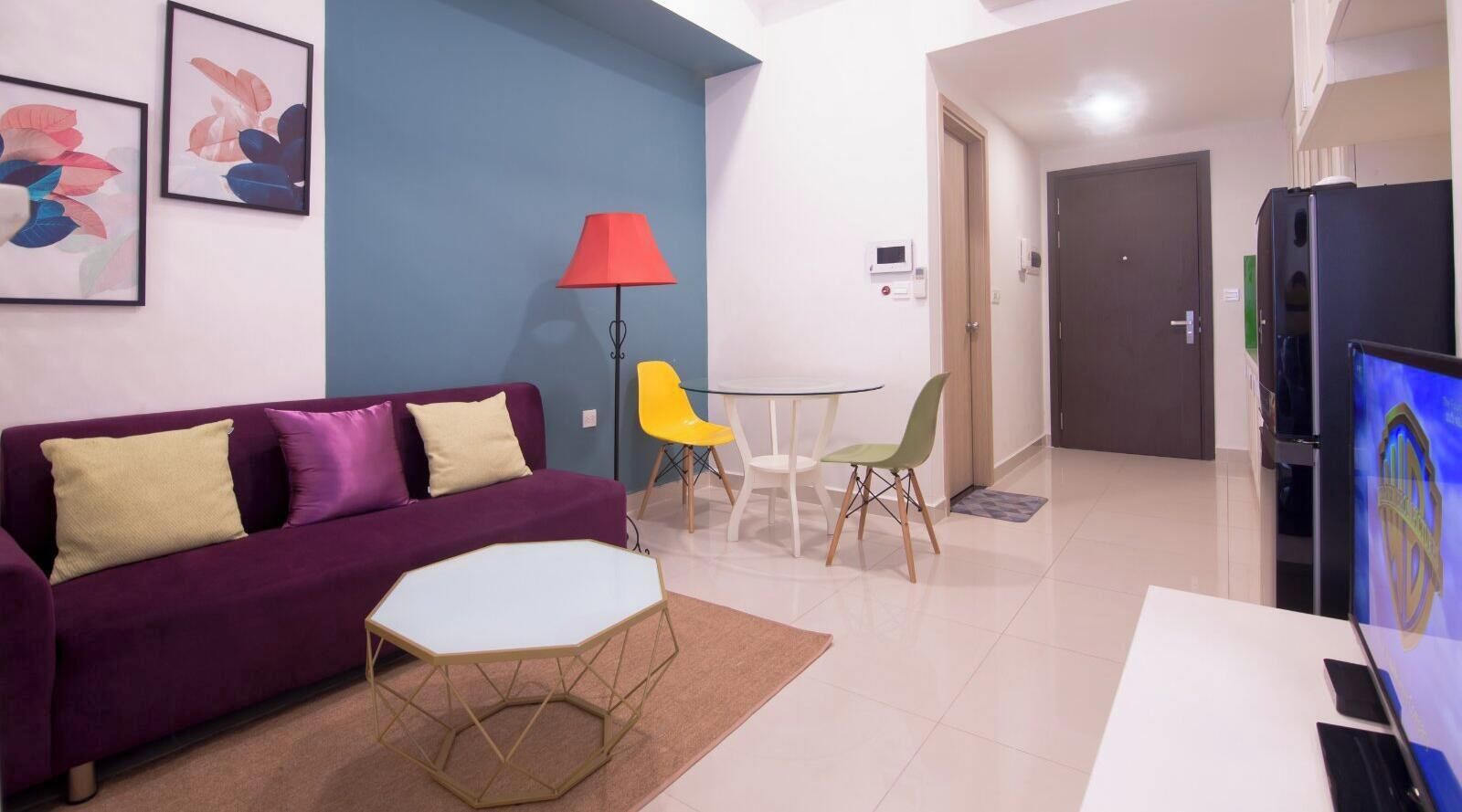 A living room with a purple sofa, a small white table, and a red lamp.