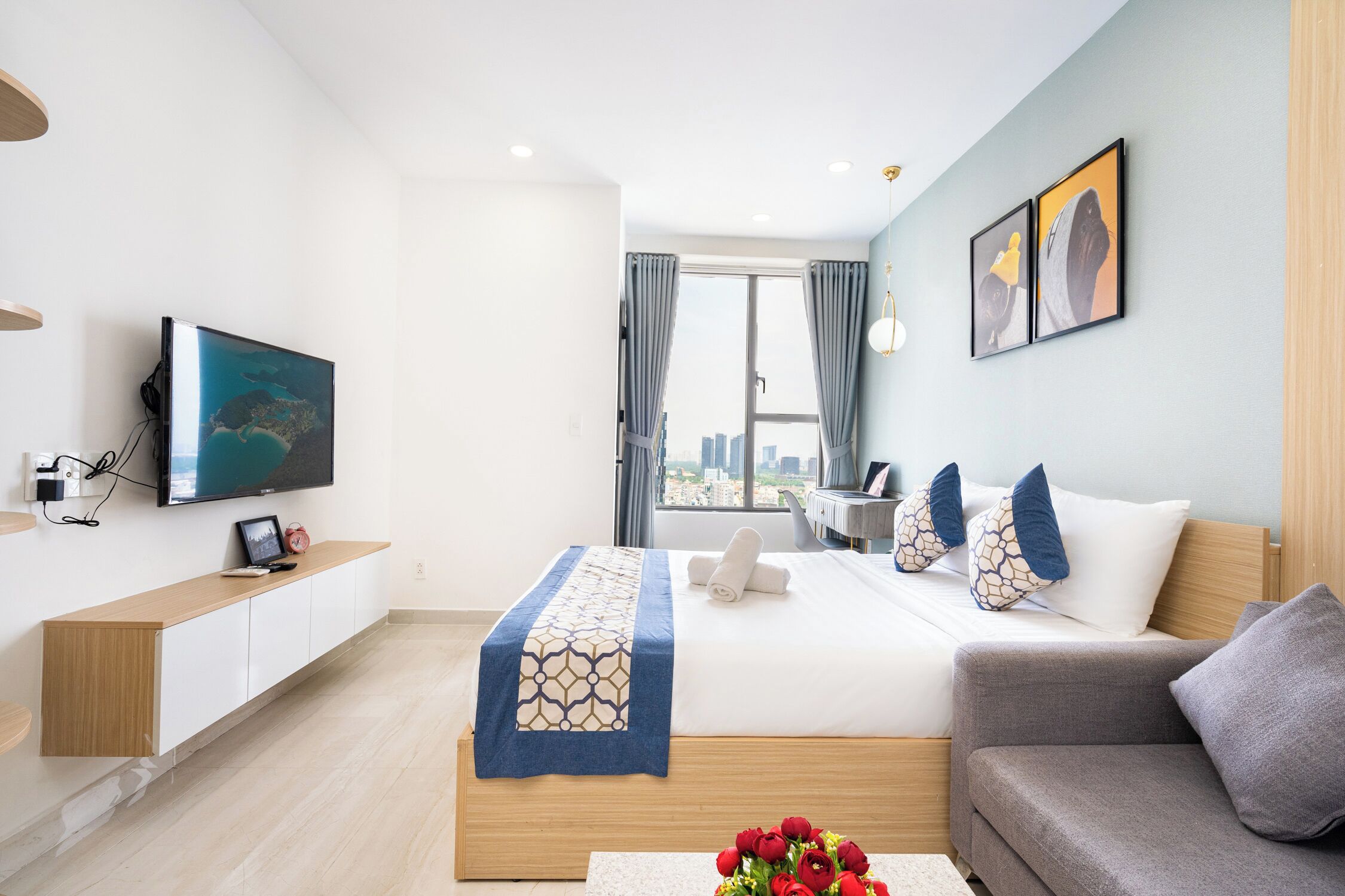 A modern hotel room with a bed, a sofa, a TV, and a city view.