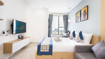 A modern hotel room with a bed, a sofa, a TV, and a city view.