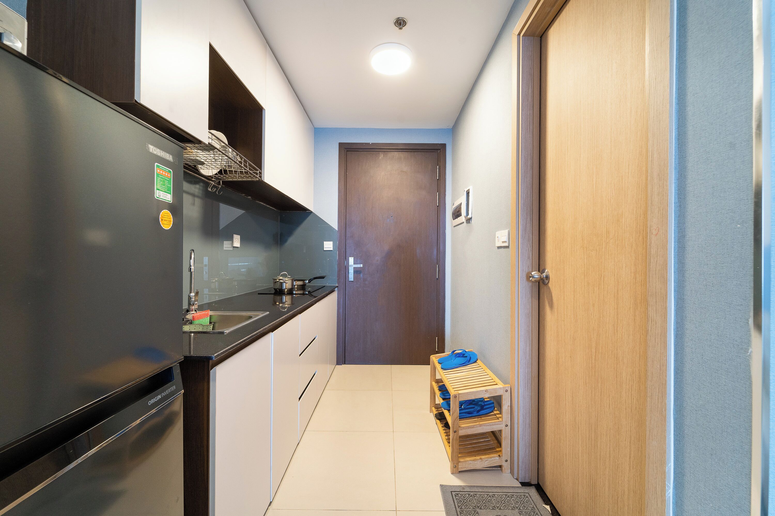 Una cocina compacta con refrigerador, pileta y una pequeña mesa de madera con vajilla.