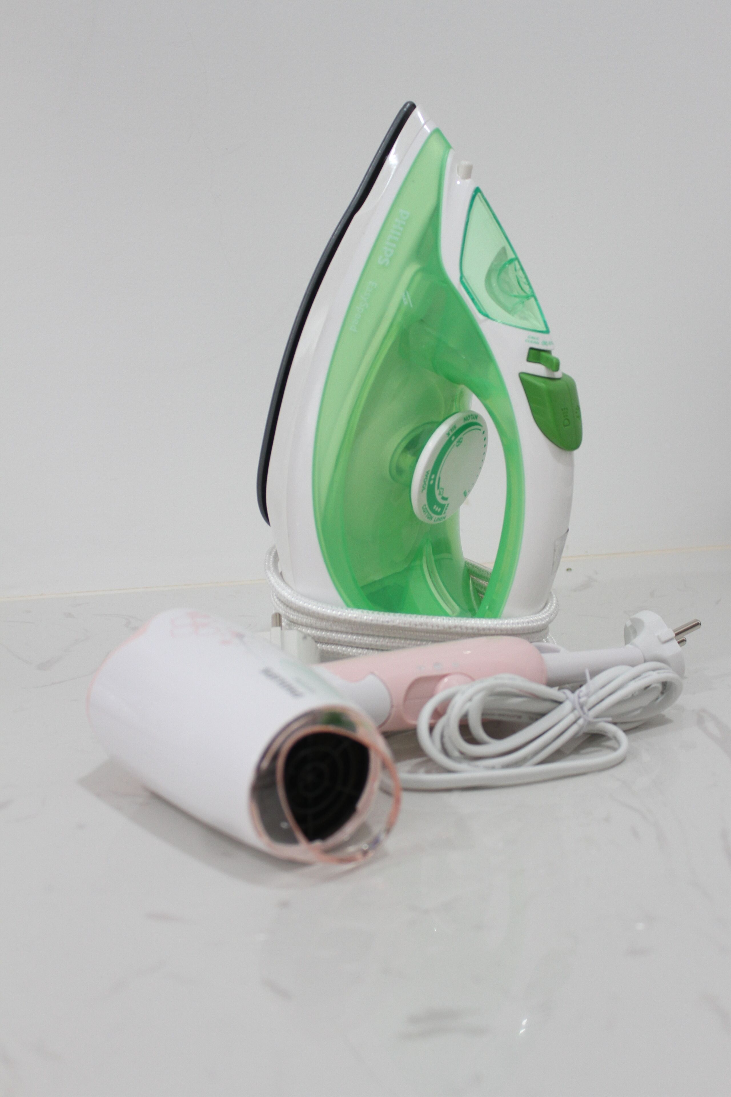 Una plancha portátil con diseño verde y blanco, un cable de alimentación y un cable de carga.