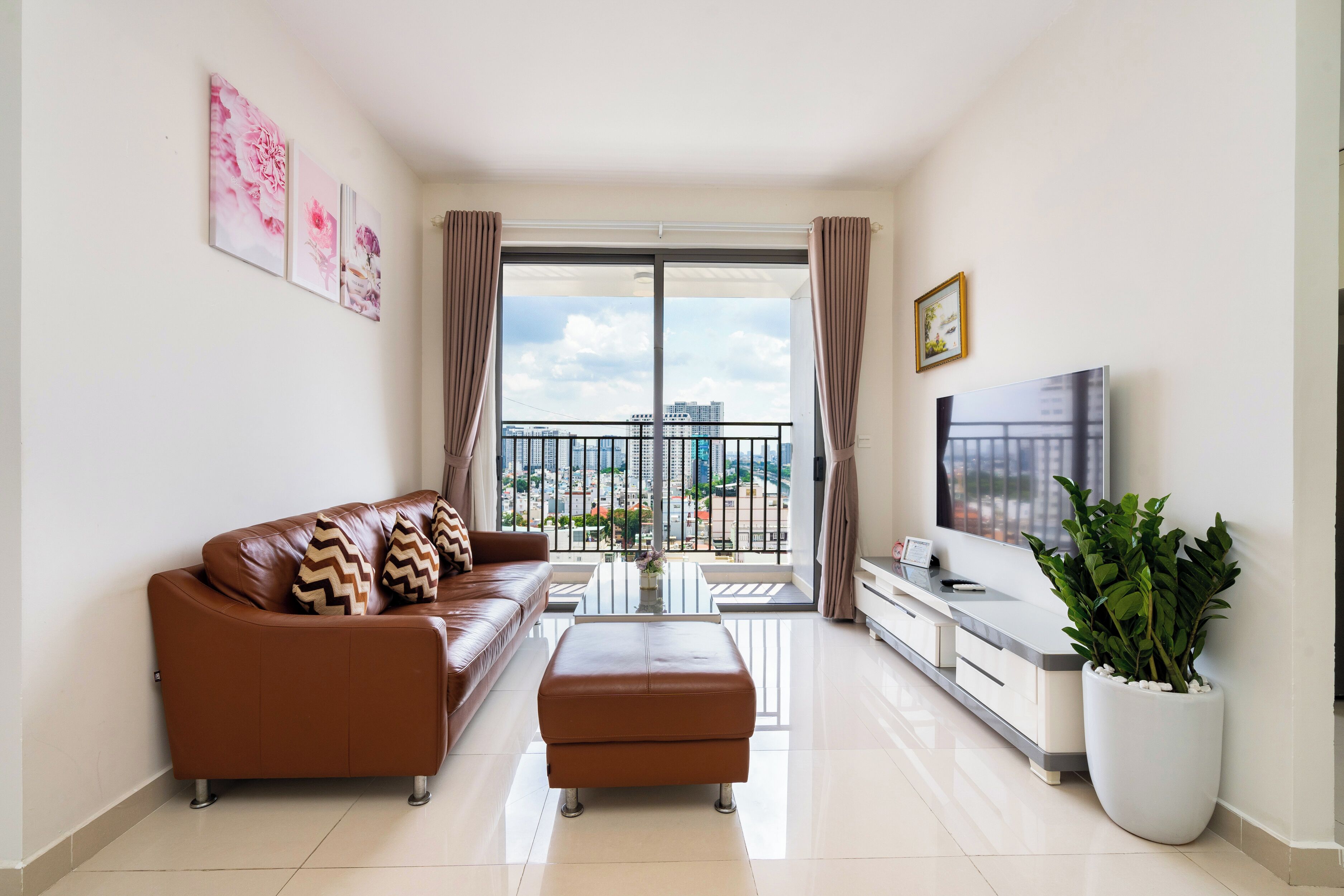 A modern living room with a brown leather sofa, a flat-screen TV, a coffee table, and a large potted plant.