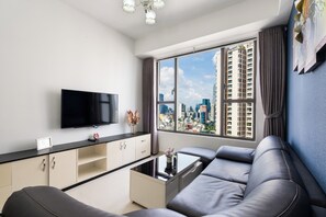 A modern living room with a flat-screen TV, a sofa, a coffee table, and a view of a cityscape through large windows. - GobyHome - Rivergate Residence Infi Pool (Ho Chi Minh City)
