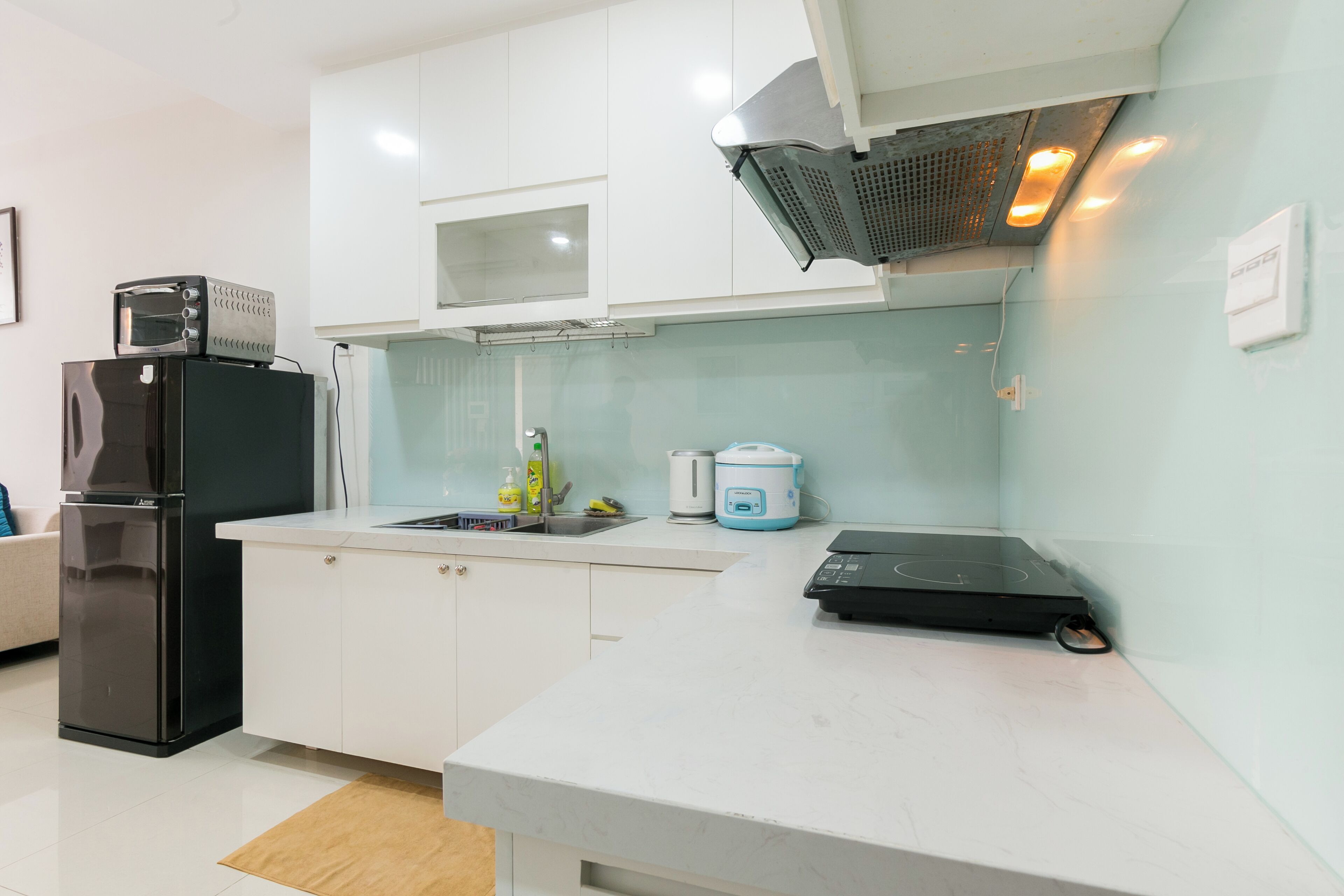 Una cocina moderna con armarios blancos, un refrigerador negro, un microondas, un tostador, un lavamanos y una cocina portátil de inducción.