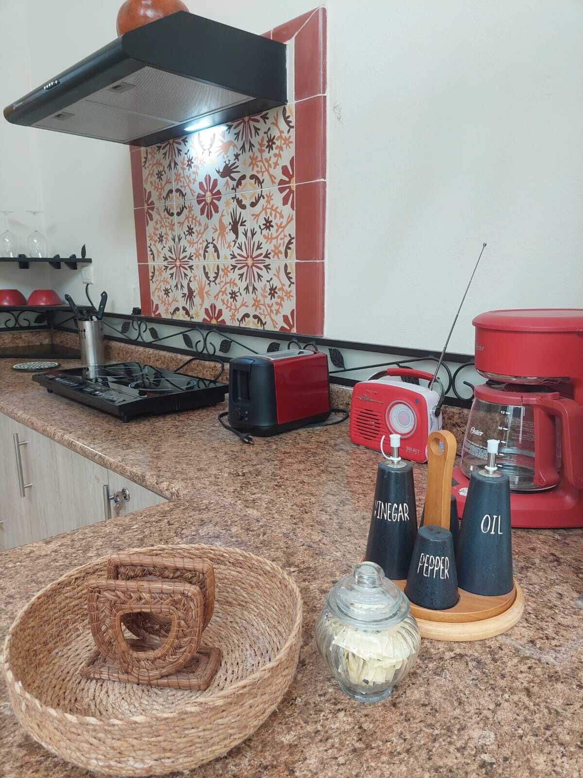 Une cuisine équipée d’une cuisinière à gaz, d’un batteur électrique rouge, d’une machine à café et de récipients à épices.