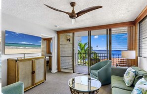 A room with a ceiling fan, a large window with a view of the beach, a sofa, and a small table. - Maui 2-bedroom condo/Kihei/Beach front/ Thanksgiving Week (Kihei)