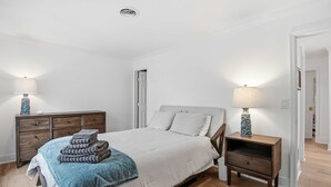 A bedroom with a bed, bedside tables, a dresser, and a door. - 3BR New Renovation, with pool, tennis, trolley! (Bethany Beach)