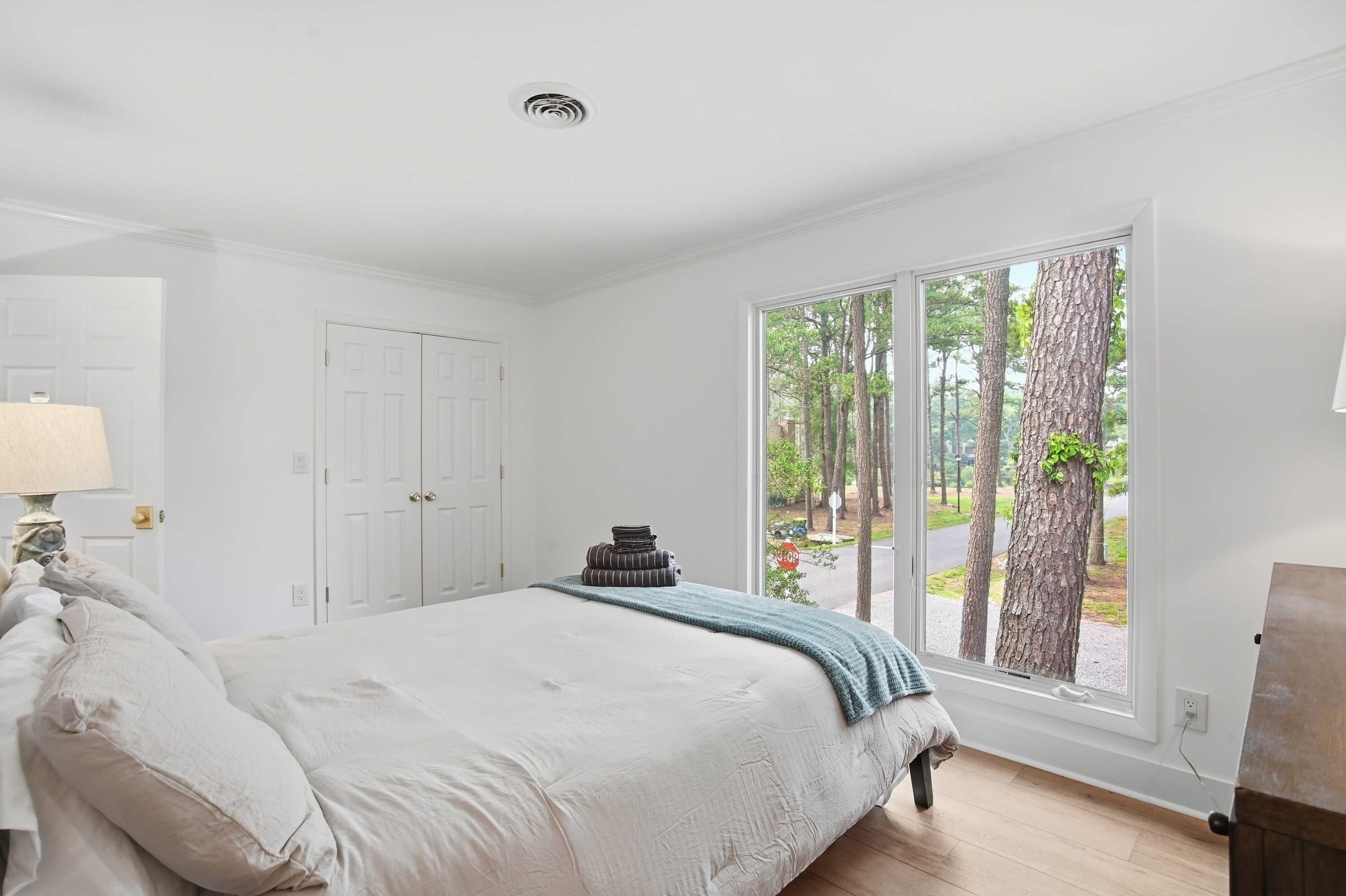 Une chambre à coucher avec un lit, une lampe, une fenêtre donnant sur des arbres et une porte.