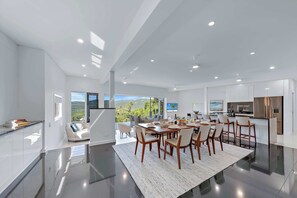 A modern kitchen with a dining area, large windows, and a view of the outdoors. - Airlie Views Luxe Escape  - Ocean Views and Pool (Airlie Beach)