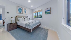Une chambre à coucher moderne avec un grand lit, une table de chevet, une lampe et des œuvres d’art accrochées aux murs.