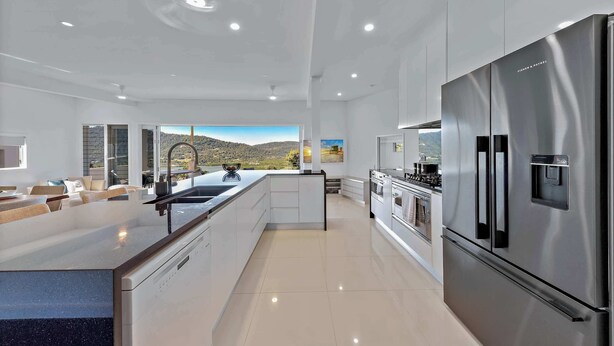 Une cuisine moderne dotée d’un grand îlot central, d’appareils électroménagers en acier inoxydable et offrant une vue sur un paysage montagneux.