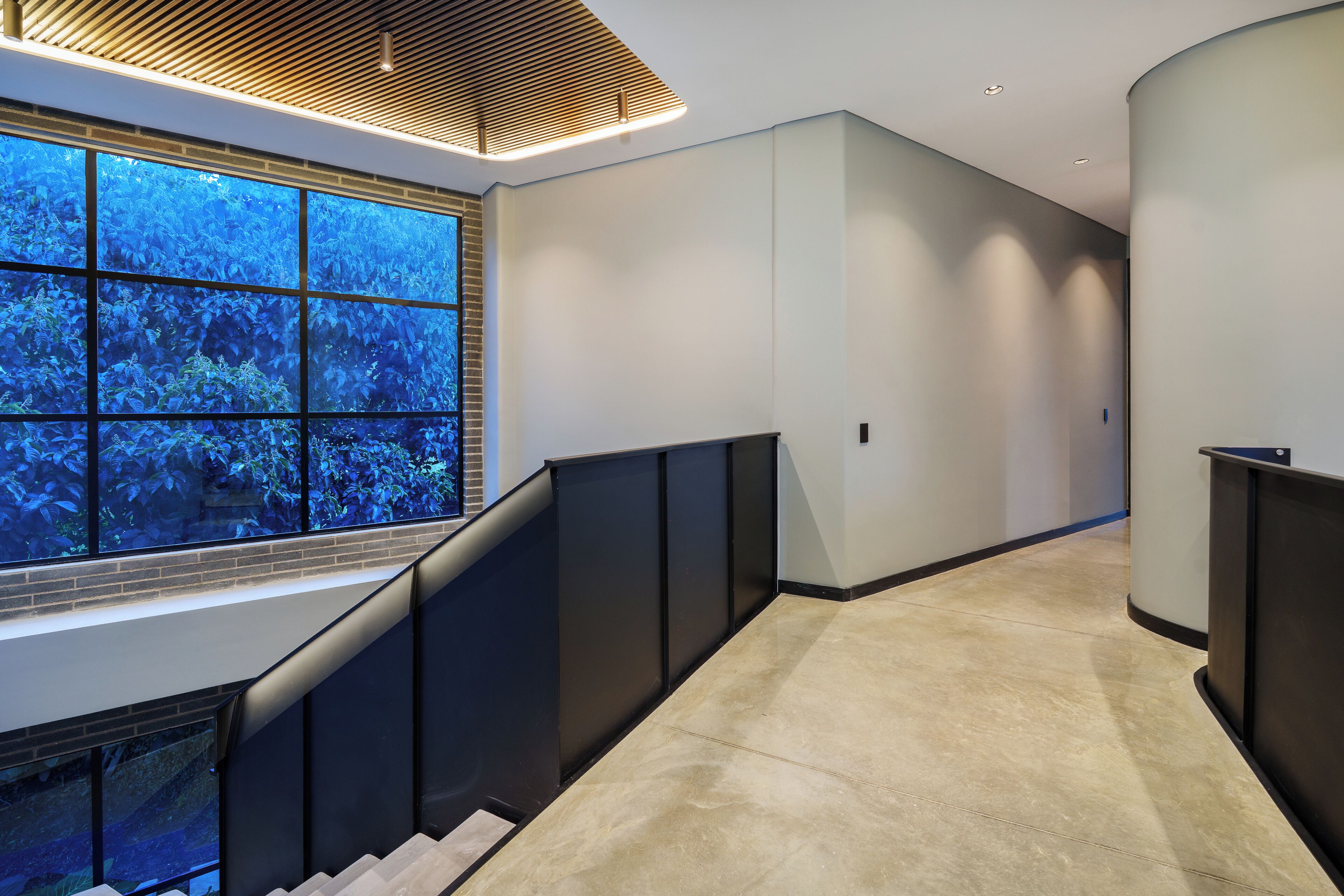 Een modern interieur met een trap, een groot raam met uitzicht op blauw groen, en een gebogen muur.