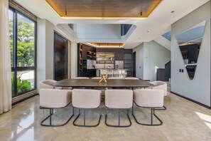 Una cocina moderna con electrodomésticos integrados, un comedor con una mesa grande y sillas, y vistas al exterior a través de amplios ventanales.