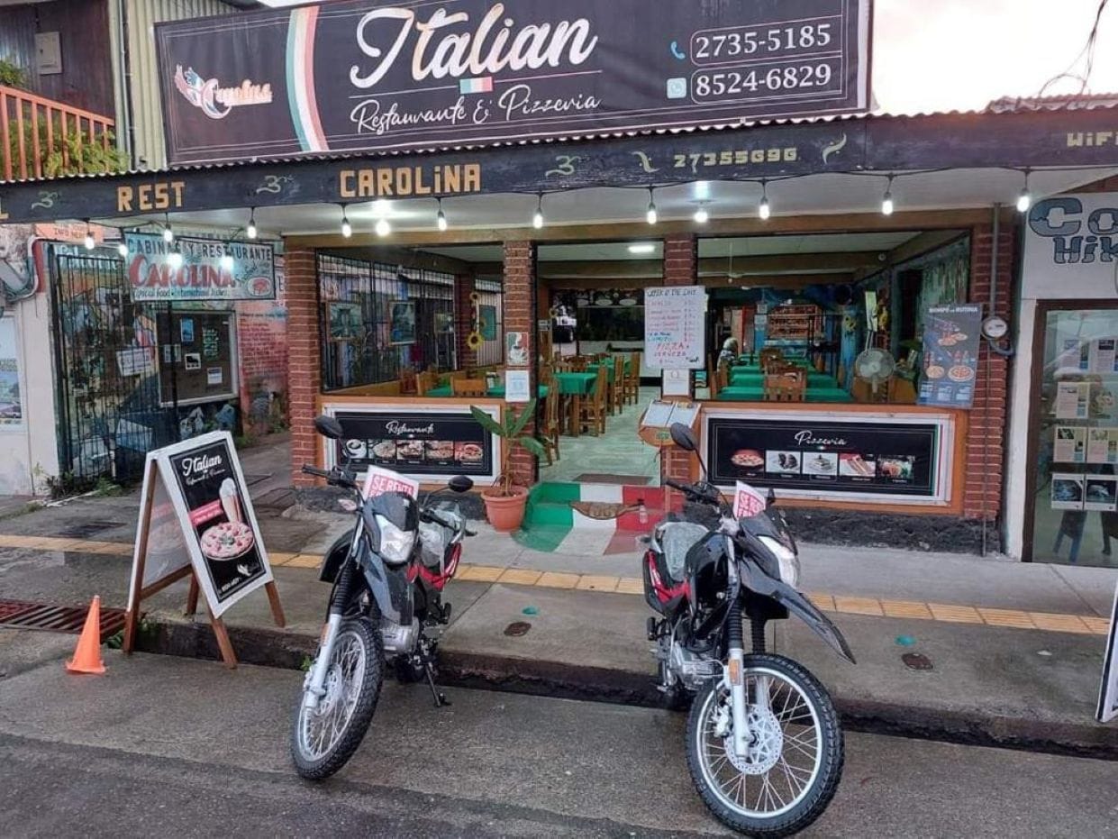 Un restaurante llamado 'Italian Restaurant & Pizzeria' con terraza y un cartel que anuncia una oferta especial.