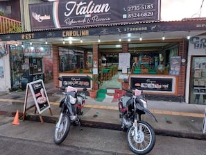 Un restaurante llamado 'Italian Restaurant & Pizzeria' con terraza y un cartel que anuncia una oferta especial.