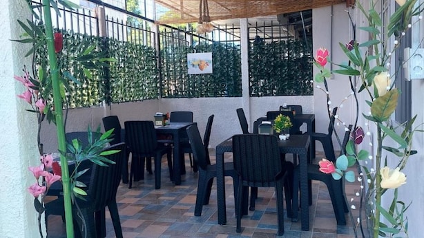 Terrassa exterior amb taules i cadires, envoltada per una tanca i plantes en testos.