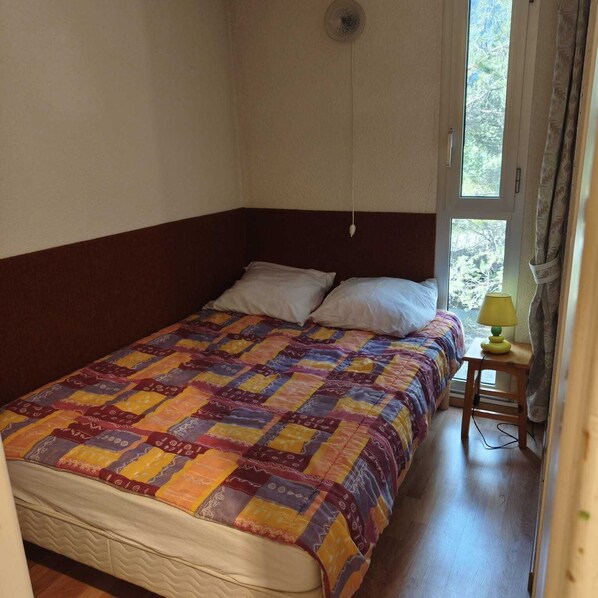 A single bed with a colorful quilt, a bedside lamp, and a window with curtains.