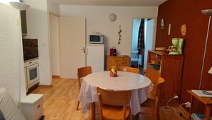 A compact living space with a dining table, chairs, a kitchenette, and a small television.