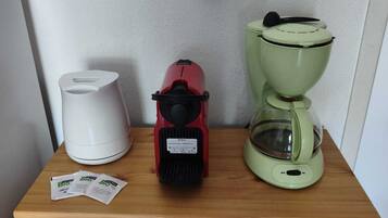 Een houten kastje met een witte koffiezetapparaat, een rode elektrische waterkoker en een groene koffiepot.