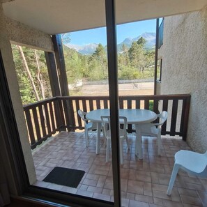 A covered outdoor patio with a table and chairs, a view of mountains, and a wooden railing. - Appart 3 chambres avec balcon – Résidence de l’Ubaye, Le Sauze (Le Sauze)