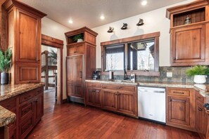 A kitchen with wooden cabinets, a dishwasher, and a window with a view. - Sandy Beach Lodge | Lakefront Luxury | 30min to YNP (Island Park)