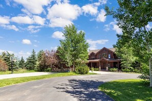 A two-story house with a front porch, surrounded by trees and a clear sky. - Sandy Beach Lodge | Lakefront Luxury | 30min to YNP (Island Park)