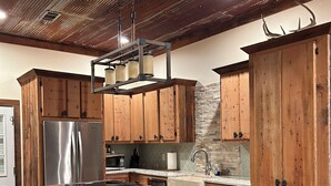 A kitchen with wooden cabinets, a stainless steel refrigerator, a wooden island with stools, and a black trash can.