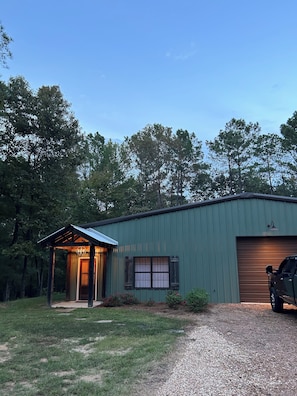 A single-story building with a covered porch, a garage, and a gravel driveway.