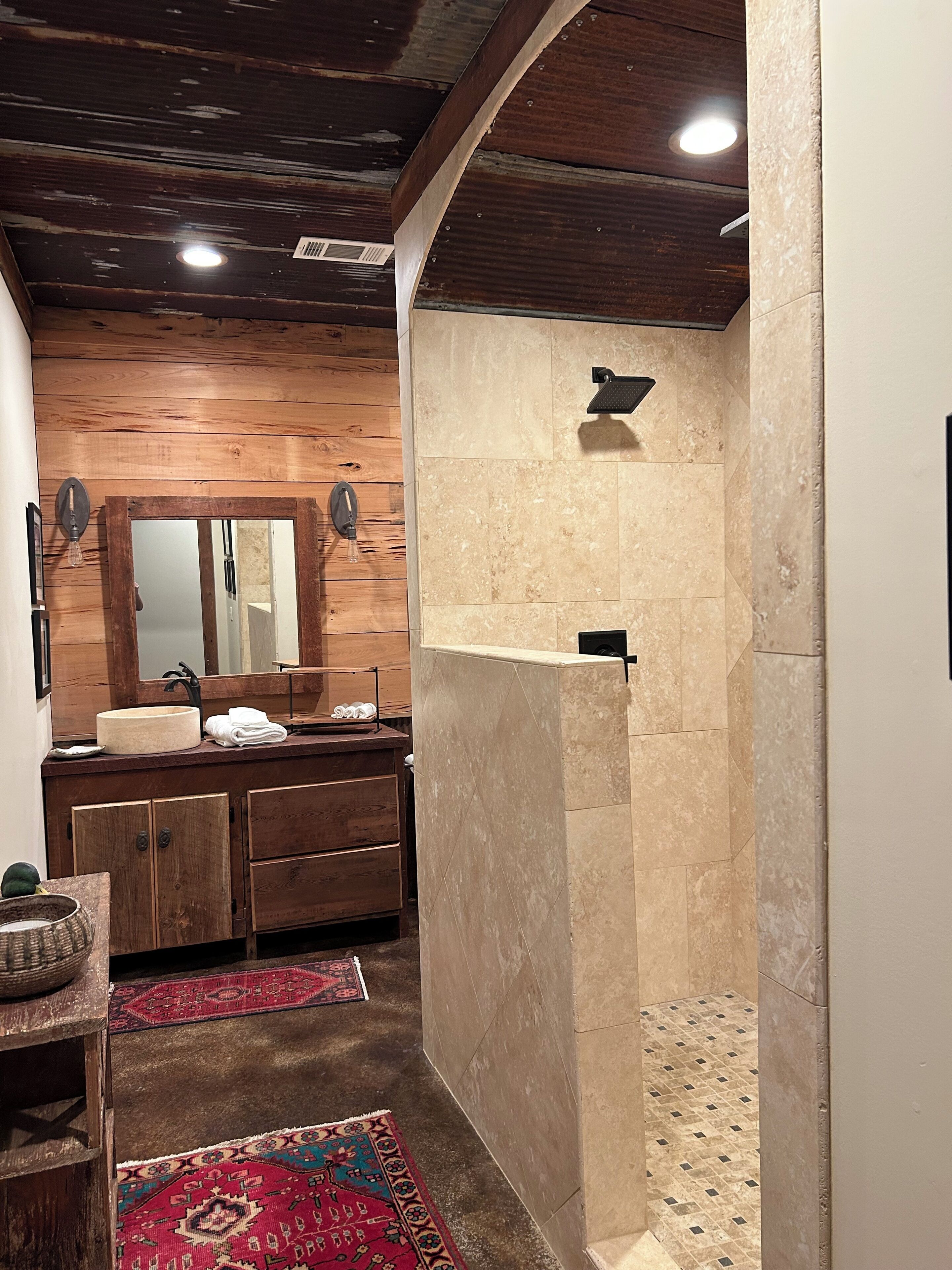 Une salle de bain avec un meuble-lavabo en bois, un miroir, un lavabo et un espace douche dont les murs sont recouverts de carreaux.