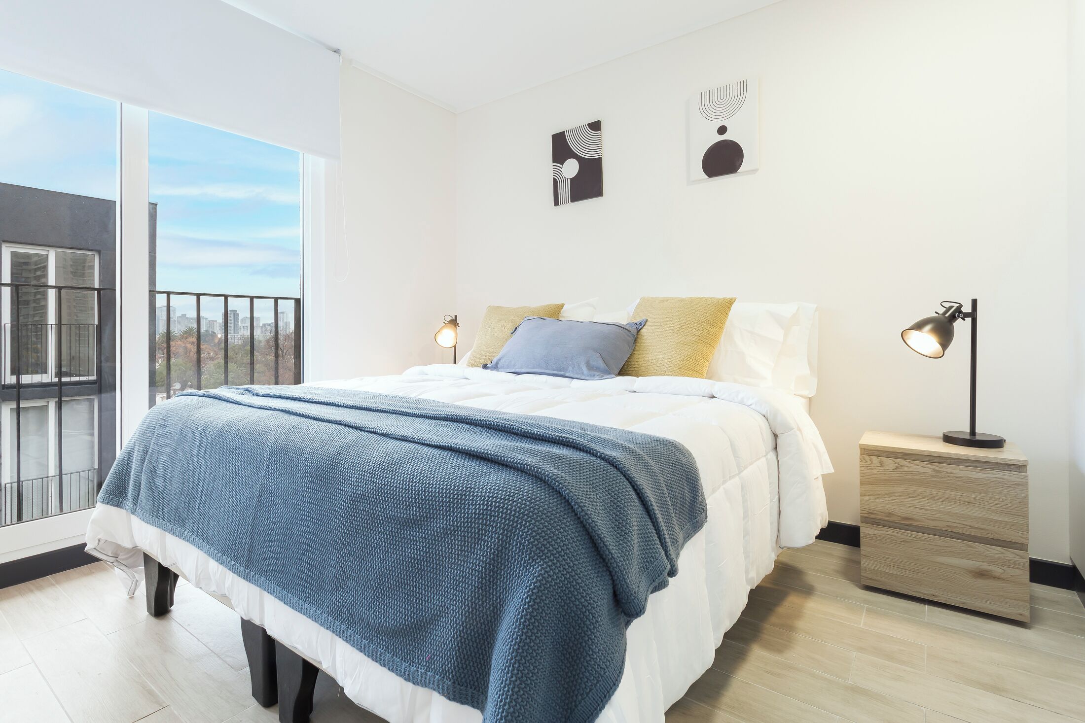 Quarto moderno com uma cama grande, uma mesa de cabeceira e vista para a cidade através de uma varanda.