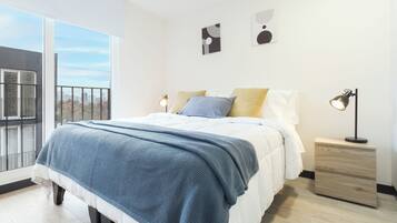 Quarto moderno com uma cama grande, uma mesa de cabeceira e vista para a cidade através de uma varanda.