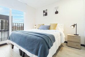 Un dormitorio moderno con una cama grande, una mesita de noche y vistas a la ciudad desde un balcón.