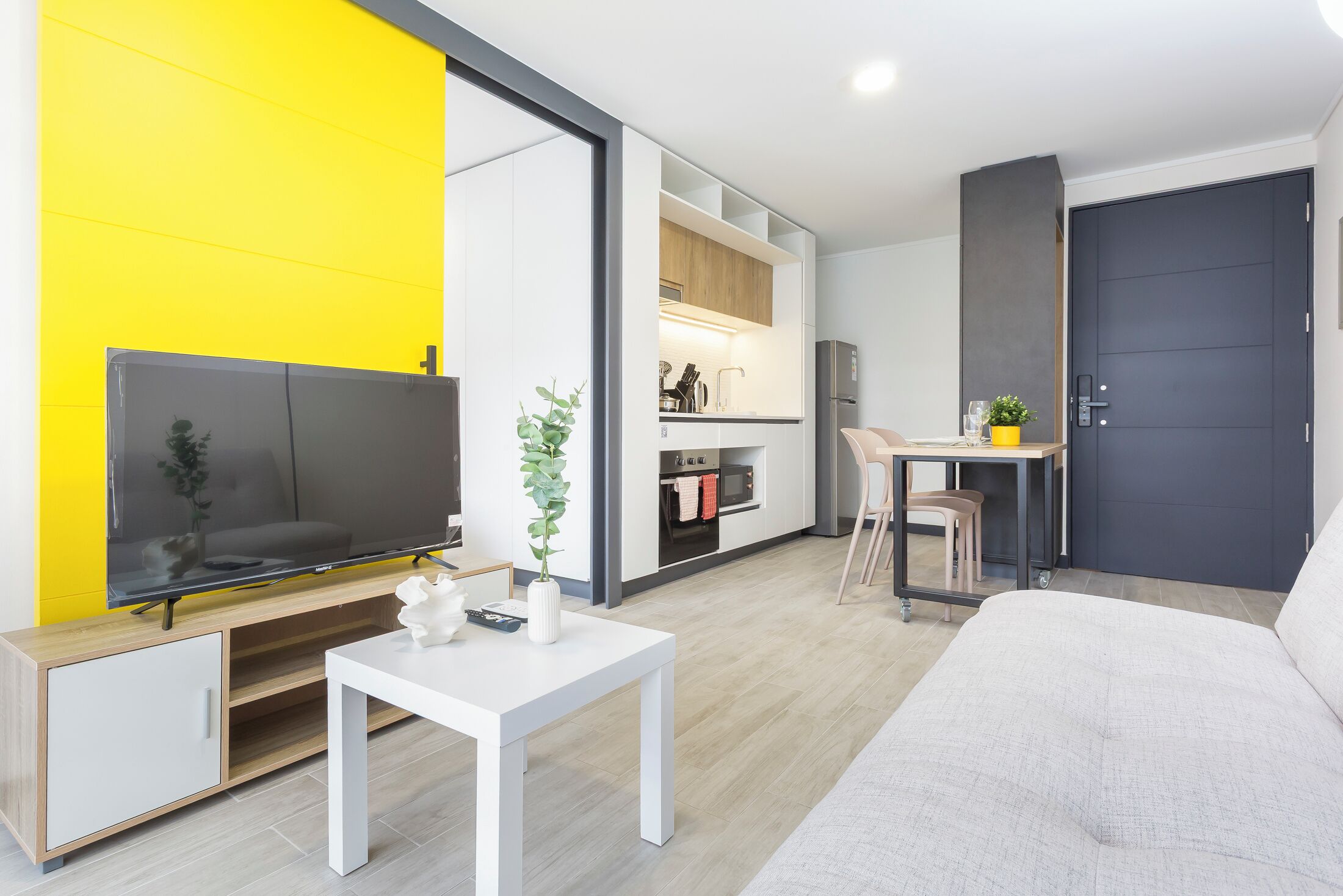 A modern living room with a flat-screen TV, a white coffee table, and a sofa.