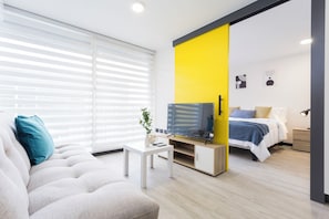 Una sala moderna con sofá, mesa de centro, televisión y cama con una pared de acento amarilla.