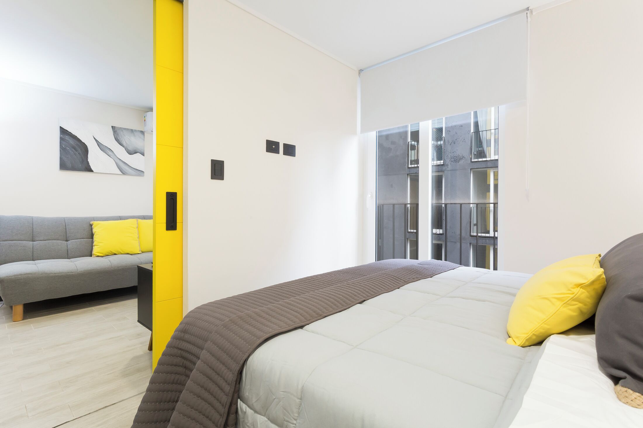 Un dormitorio moderno con cama, sofá y ventana con vistas a un edificio.