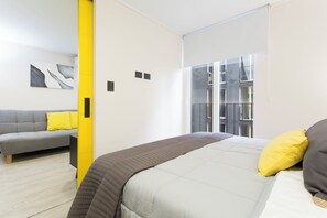 Un dormitorio moderno con cama, sofá y ventana con vistas a un edificio.