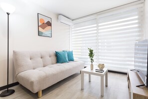 Una sala de estar moderna con un sofá, una mesa de centro, una planta y un televisor.