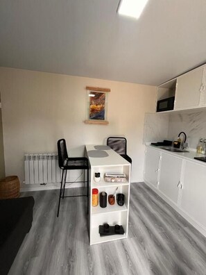 Cocina compacta con una mesa de comedor, sillas, un armario blanco y un radiador.