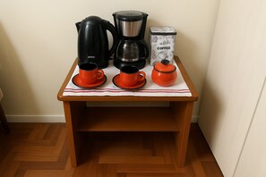 A small wooden table with a coffee maker, a kettle, and a coffee container.