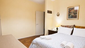 Une chambre d’hôtel avec un lit, une table, une chaise, une table de chevet, une lampe et un tableau au mur.
