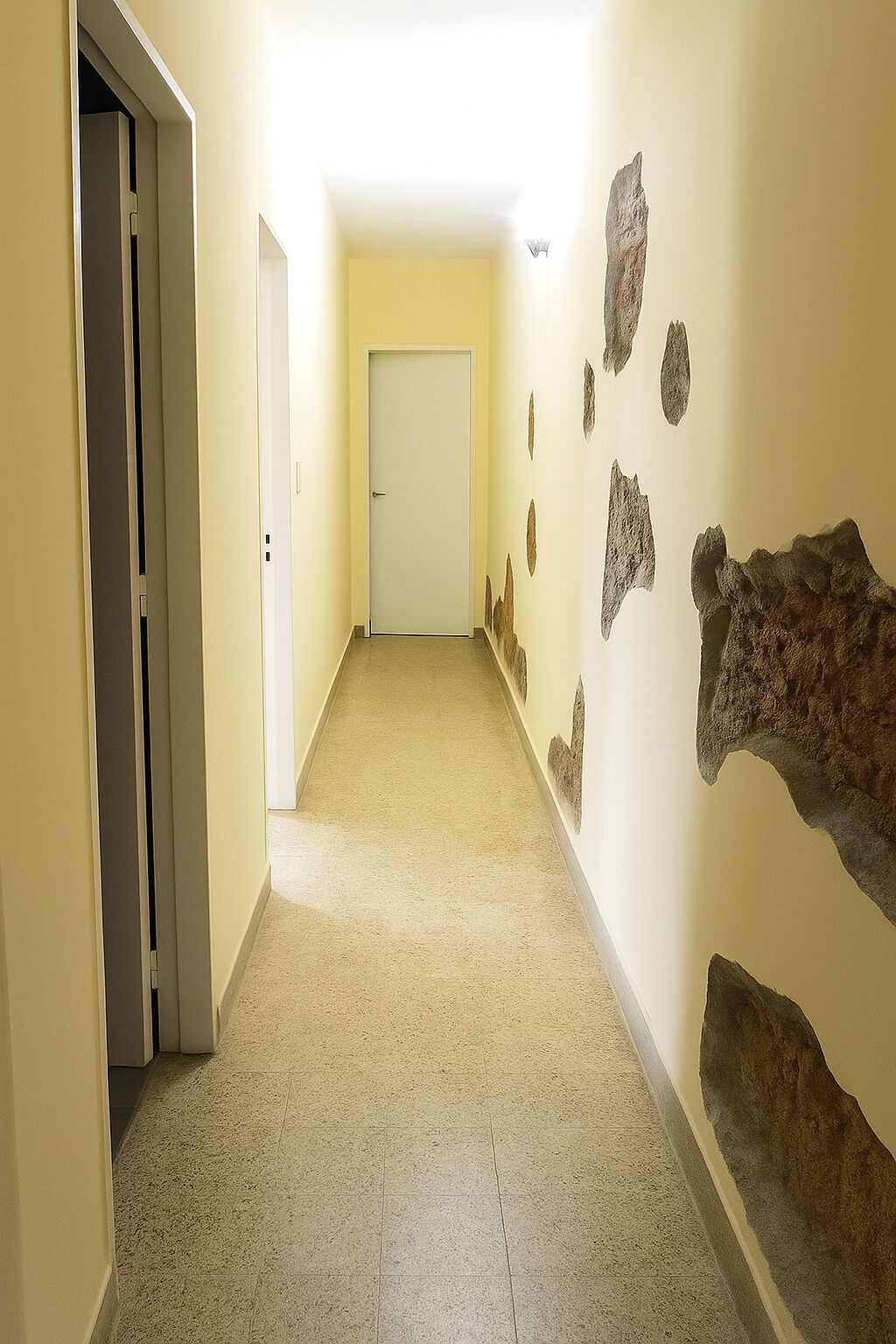 A hallway with beige walls, a carpeted floor, and a door at the end.
