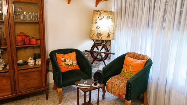 Un salon avec deux fauteuils verts, un meuble en bois, une lampe et un gouvernail de bateau.