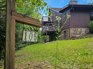 A wooden sign with the number 105, a house with a stone foundation, and a grassy hill. - Shenandoah Sky House - walk to Lake Laura trail! + fire pit (Basye)