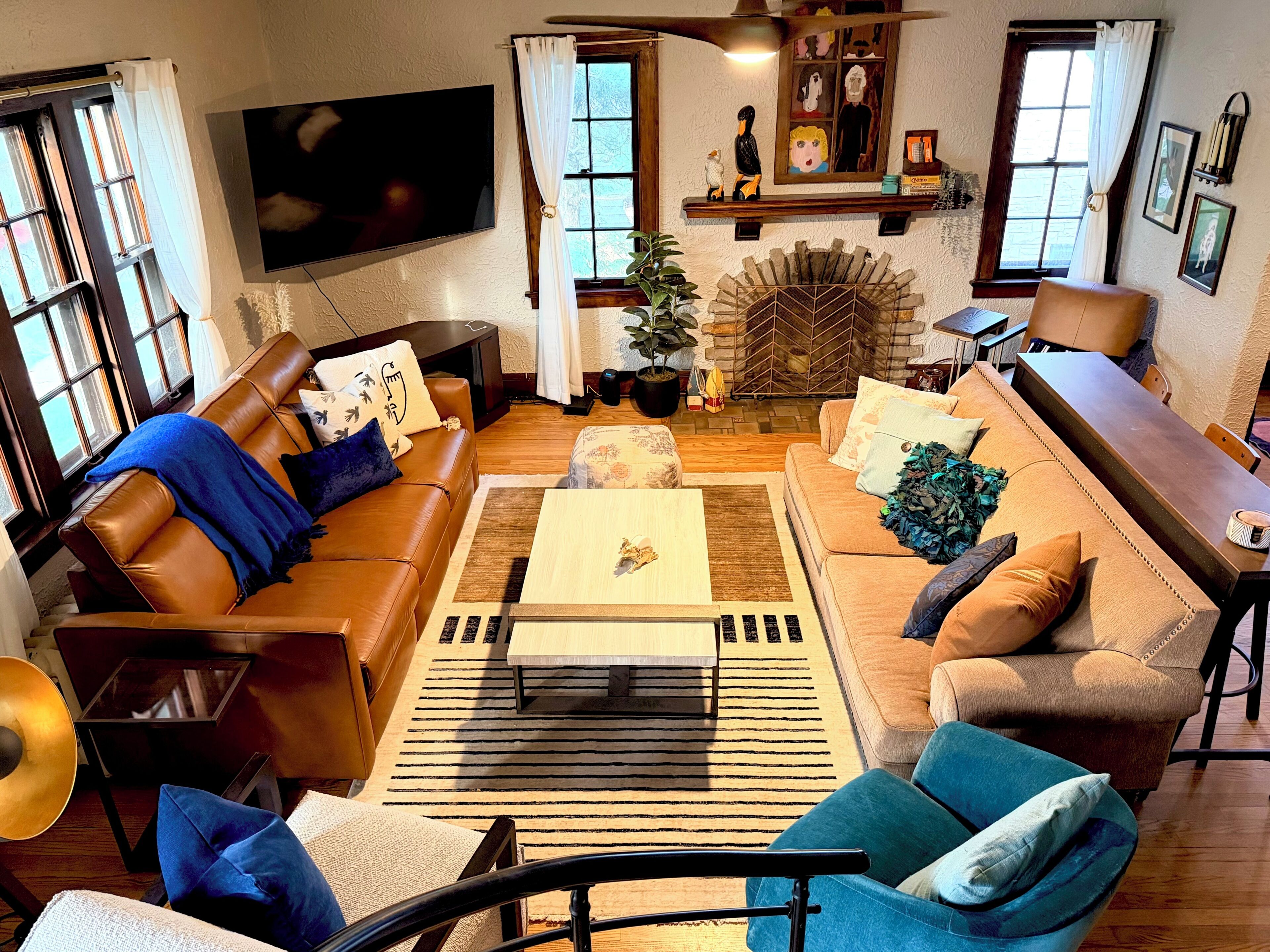 A living room with a brown leather sofa, a wooden coffee table, and a blue armchair. There is a television mounted on the wall and a fireplace with a decorative mantle.