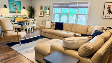 A modern living room with a beige sofa, a coffee table, and a dining area with a white table and chairs.