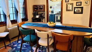 Un comedor con una mesa de madera, camino de mesa azul y sillas. Se ve una cocina al fondo.