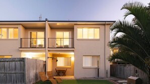 A two-story residential building with a balcony on the upper floor, a fenced backyard, and a small patio area with outdoor furniture. - Oceans 1, Beach Views, 3-Min Walk to Birubi Beach (Anna Bay)